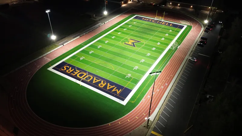 High school football field and track lit up at night, seen from above